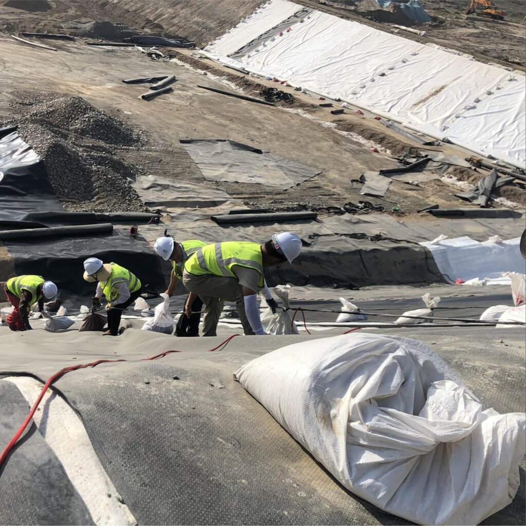 Workers positioning geomembrane panels on a tailings facility slope