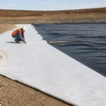 Worker installing a nonwoven geotextile cushion beside an HDPE geomembrane liner
