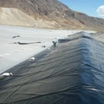 Geomembrane installation beside an exposed protective layer in an earthworks basin