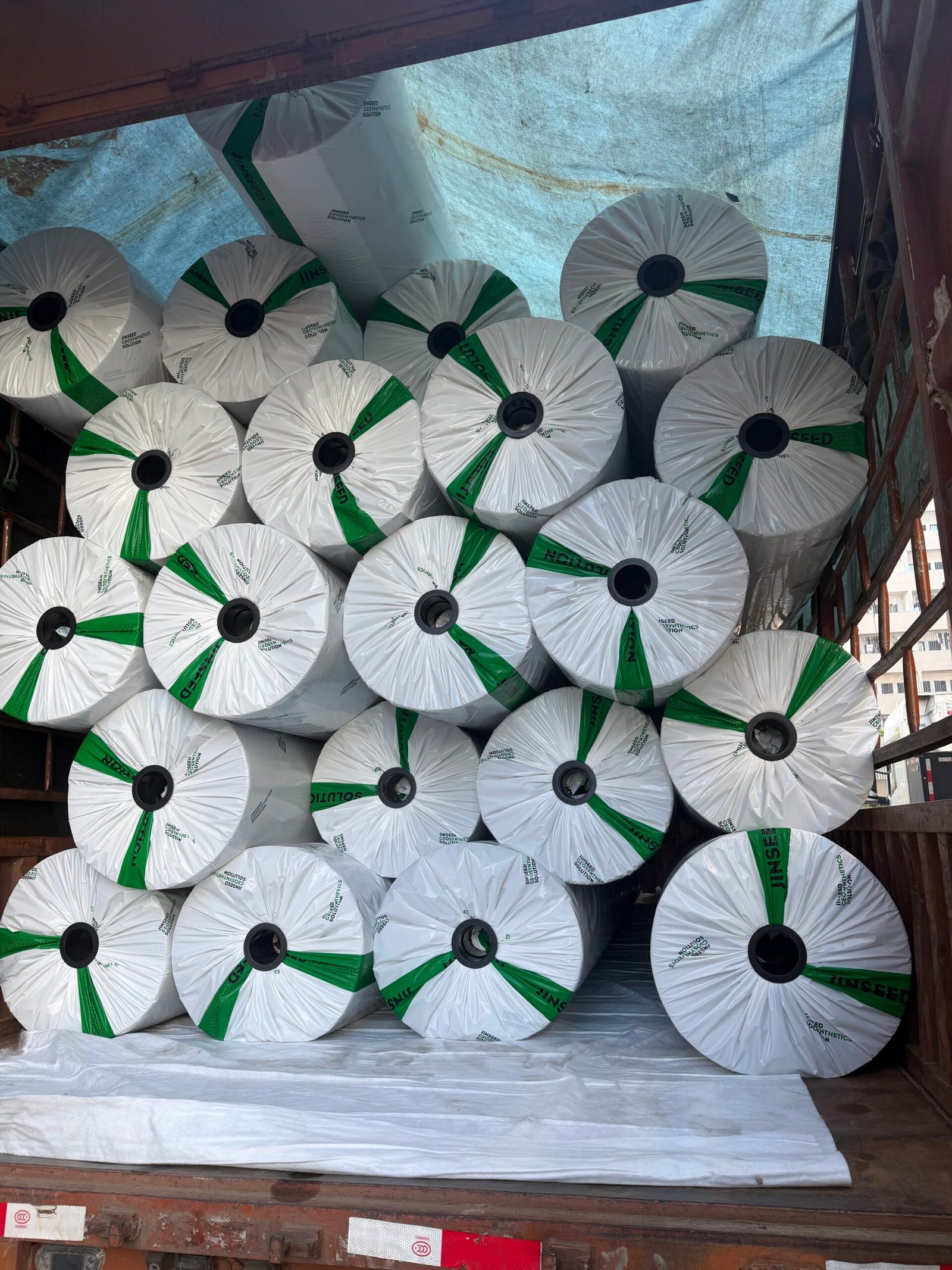 Jinseed-branded wrapped geotextile rolls stacked on a truck under a protective tarpaulin