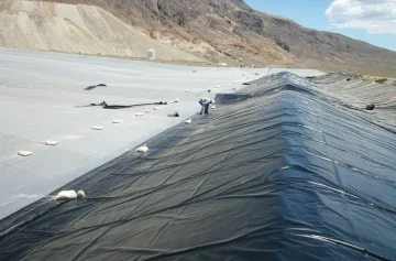 Geomembrane installation beside an exposed protective layer in an earthworks basin